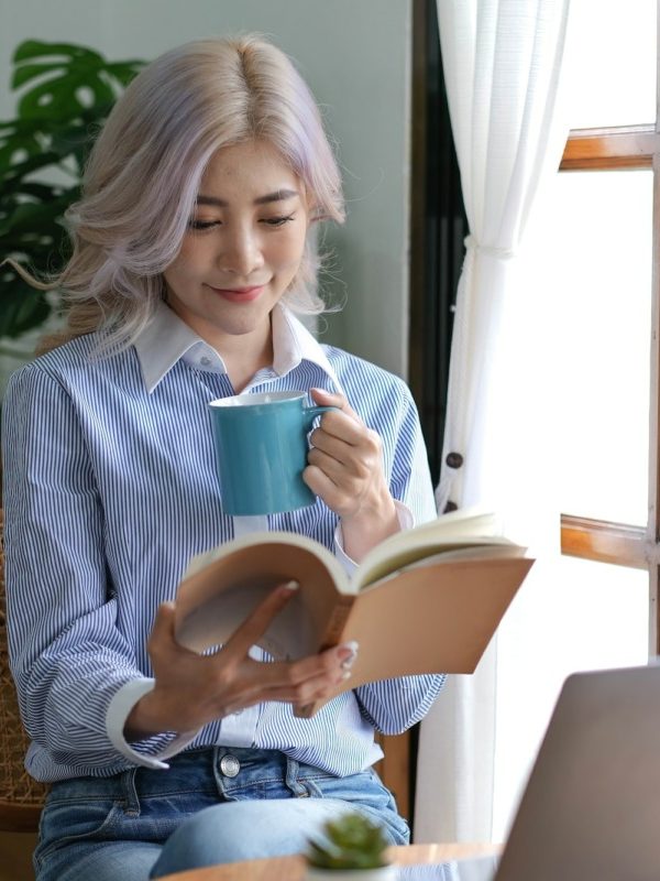 Asian woman reading a book and drinking coffee in the morning.